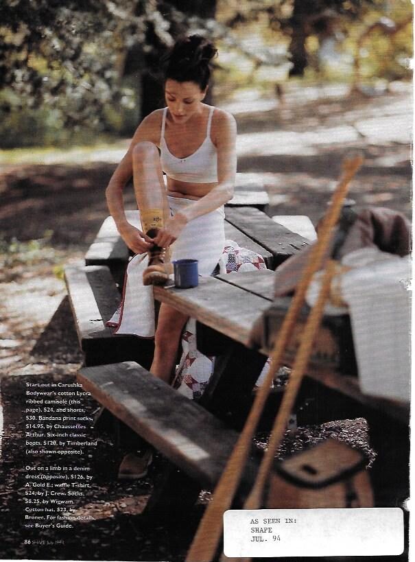 A model wearing a white Carushka ribbed cotton Lycra camisole and shorts in a rustic outdoor setting, as seen in Shape Magazine, July 1994. The image highlights the brand's versatility in lifestyle and fitness fashion.