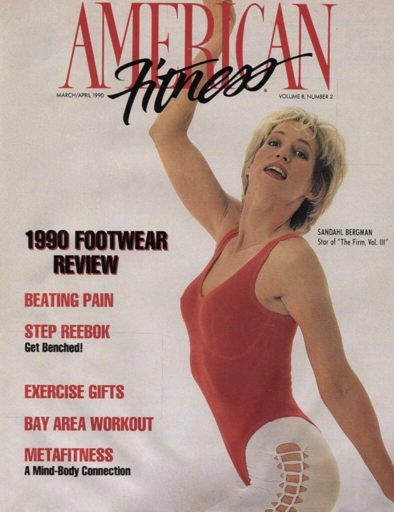 March/April 1990 cover of American Fitness magazine featuring actress and fitness star Sandahl Bergman. She is pictured in a wide athletic stance wearing a Carushka Bodywear contoured tank thong leotard in vibrant Red, beautifully contrasted with white ankle-length web-patterned leggings. The cover text highlights features on "1990 Footwear Review" and "Metafitness," celebrating the intersection of high-fashion dance aesthetics and 90s fitness culture.